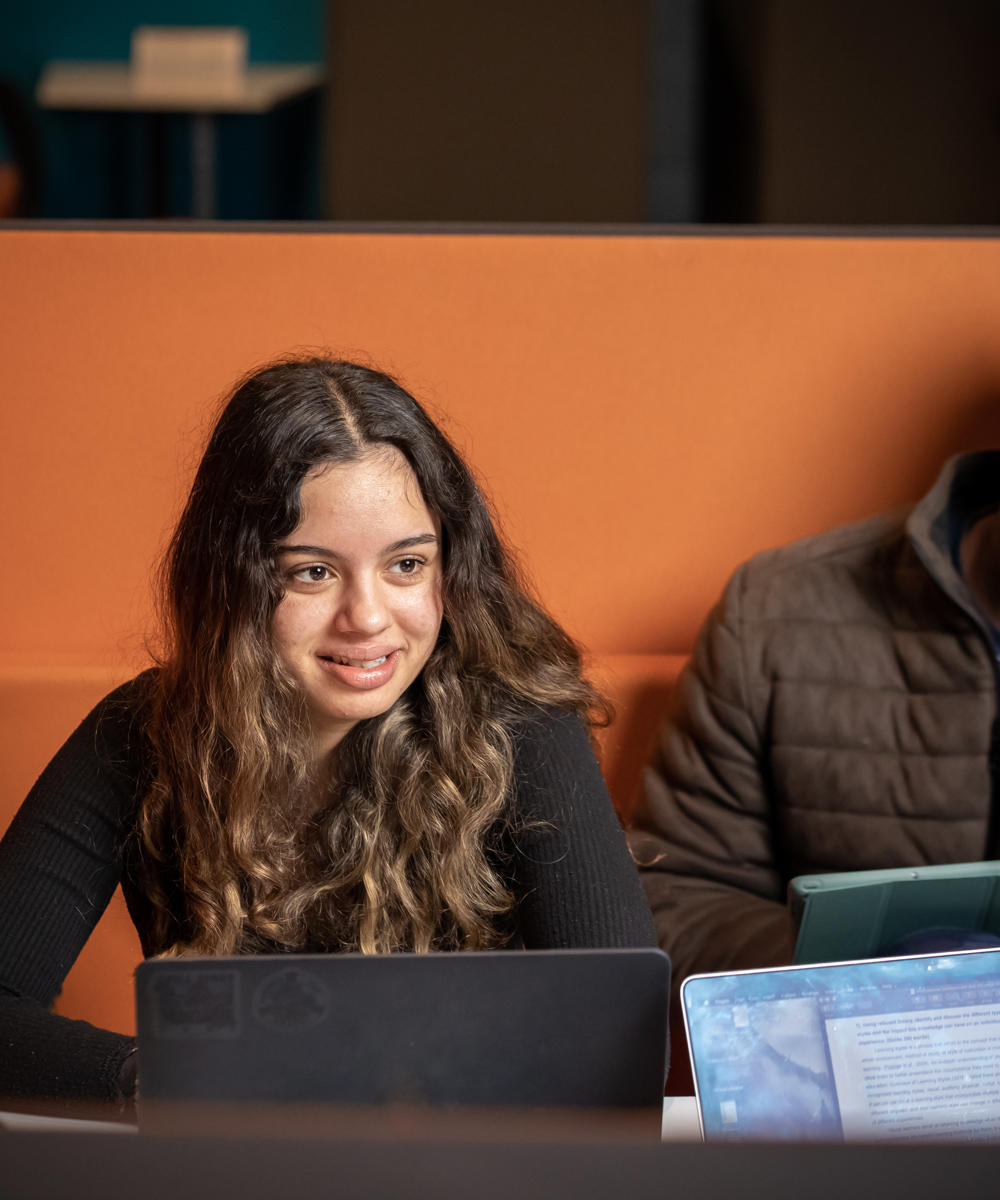 Image of a group of international students sat at a table talking with their laptops