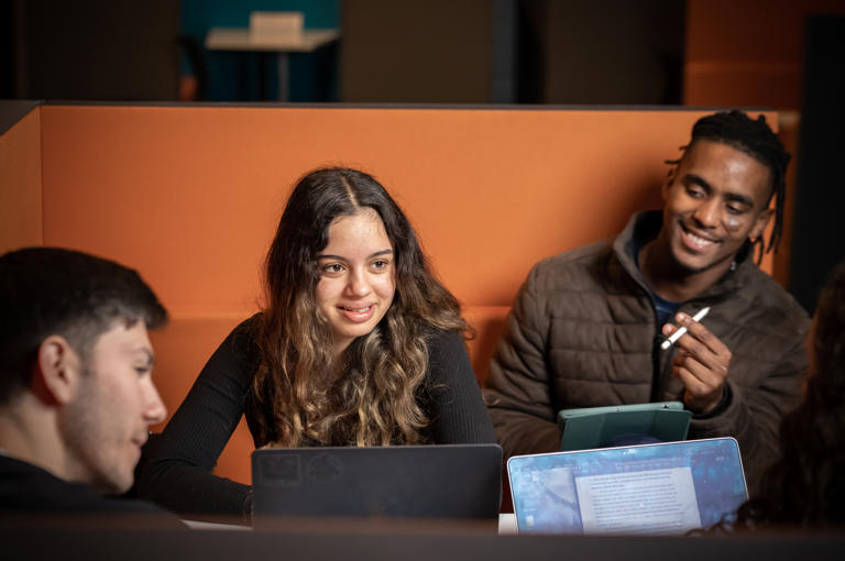 Image of a group of international students sat at a table talking with their laptops
