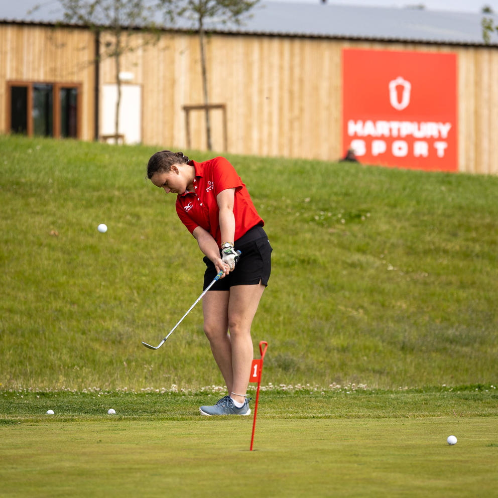 Female Student Practising In Short Game Golf Area