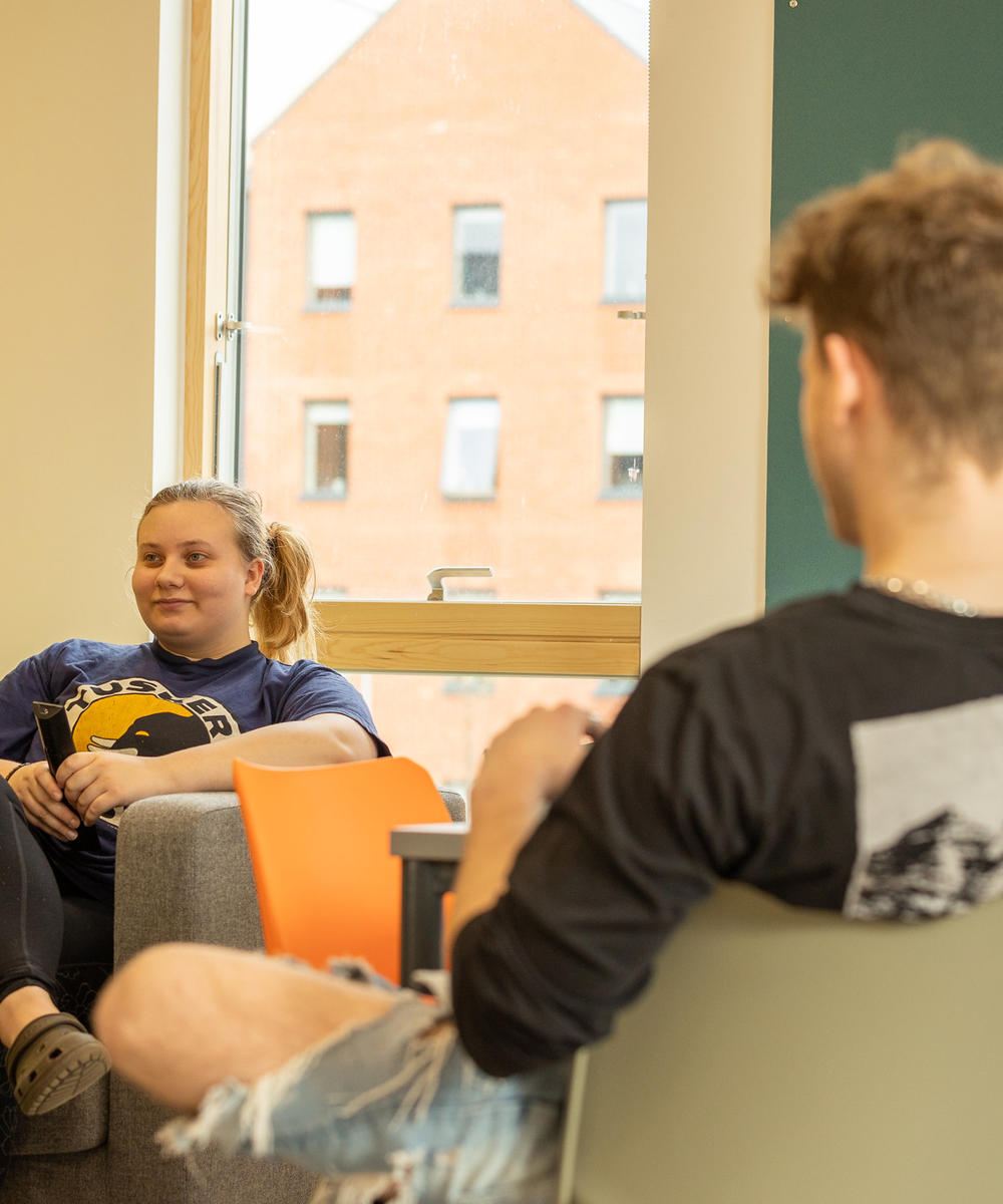 Blackfriars living space, a male and female student sat opposite chatting